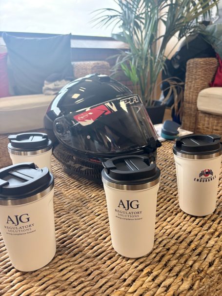Reusable travel cups funded by AJG Regulatory Solutions AJG Regulatory Solutions and Insurance Endurance branded reusable travel cups beside a racing helmet.